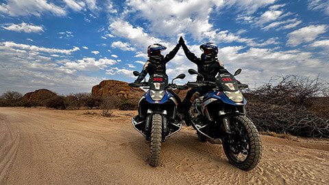 Two riders on the French women’s team sit next to one another on their R 1300 GS Competition Bikes and exchange high-fives.